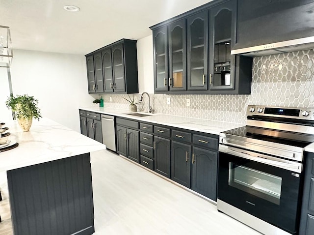 kitchen with tasteful backsplash, sink, light stone counters, stainless steel appliances, and wall chimney exhaust hood