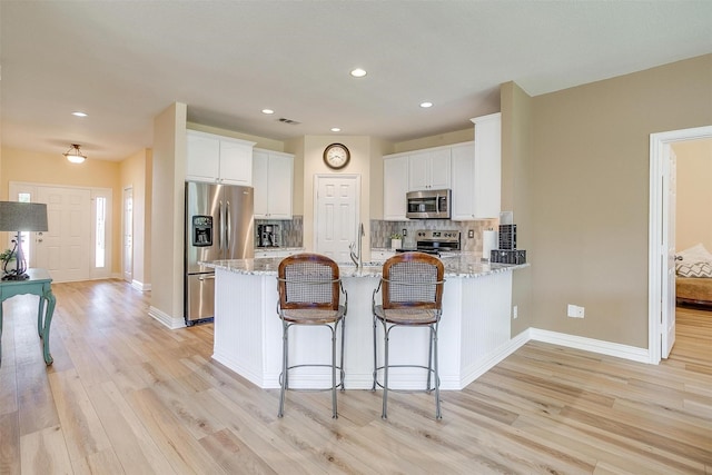 kitchen featuring stainless steel appliances, white cabinets, light stone counters, and kitchen peninsula