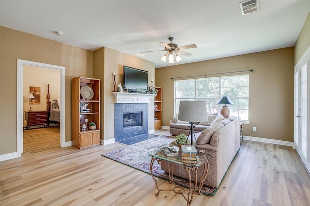 living room with a tiled fireplace, light hardwood / wood-style floors, and ceiling fan