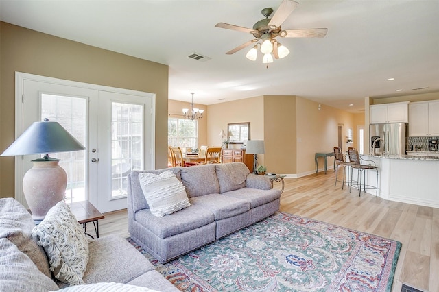 living room with ceiling fan with notable chandelier, light hardwood / wood-style floors, and french doors