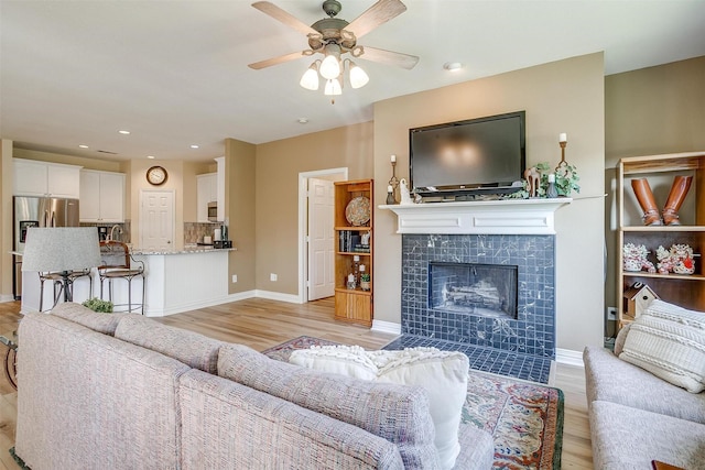 living room featuring a tiled fireplace, ceiling fan, and light hardwood / wood-style flooring