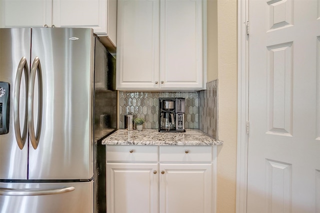 kitchen with white cabinetry, stainless steel fridge with ice dispenser, decorative backsplash, and light stone counters