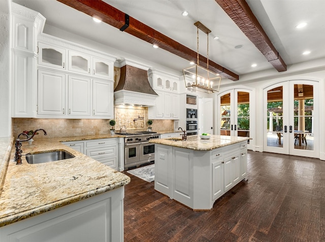 kitchen with french doors, premium range hood, sink, appliances with stainless steel finishes, and a kitchen island with sink