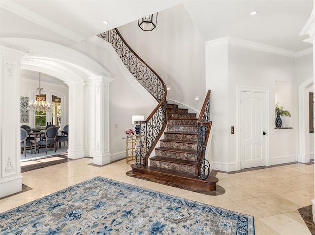 entryway featuring an inviting chandelier, ornamental molding, decorative columns, and a high ceiling