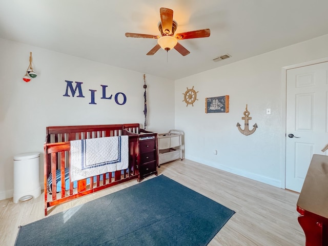 bedroom featuring hardwood / wood-style flooring, a nursery area, and ceiling fan