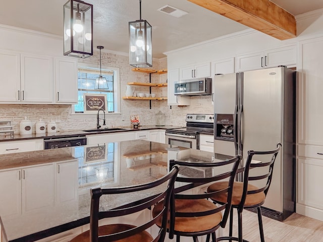 kitchen featuring appliances with stainless steel finishes, white cabinetry, sink, a kitchen breakfast bar, and crown molding