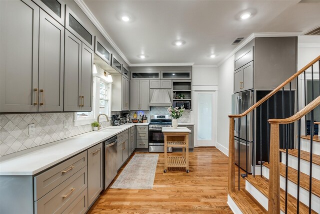 kitchen featuring light hardwood / wood-style flooring, gray cabinets, premium range hood, stainless steel appliances, and ornamental molding