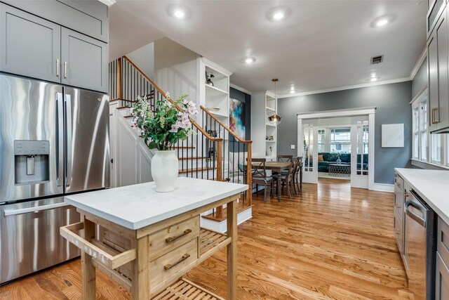 kitchen featuring pendant lighting, gray cabinetry, stainless steel appliances, crown molding, and light hardwood / wood-style flooring