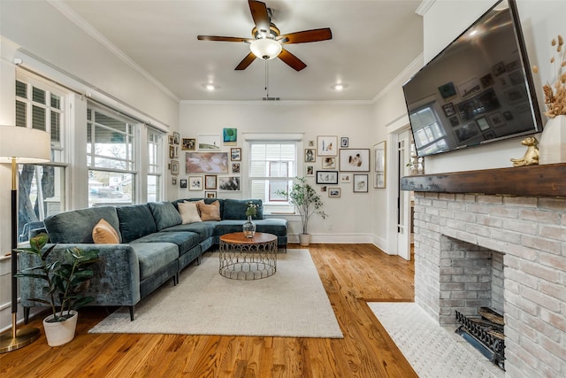 living room featuring crown molding, a brick fireplace, ceiling fan, and light hardwood / wood-style flooring