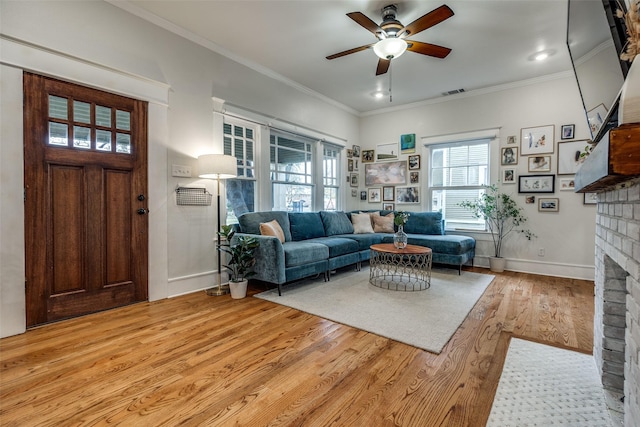 living room with a brick fireplace, crown molding, light hardwood / wood-style flooring, and ceiling fan