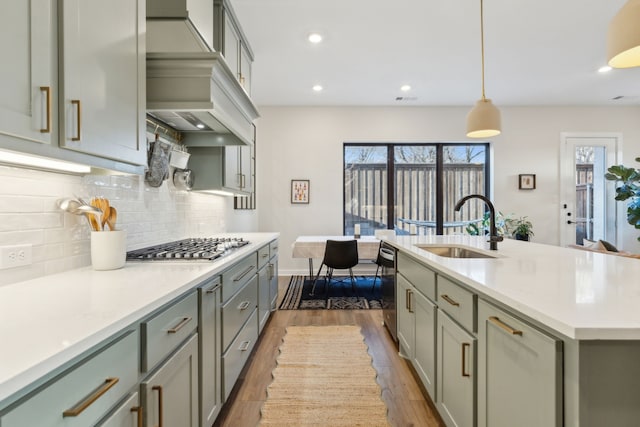 kitchen with wood finished floors, light countertops, premium range hood, stainless steel gas cooktop, and a sink