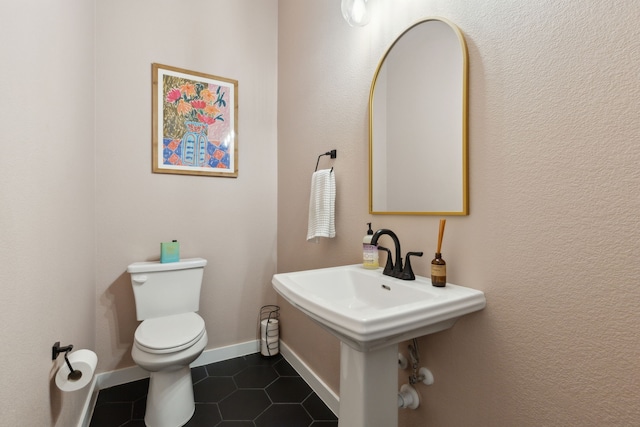 half bathroom with baseboards, a sink, toilet, and tile patterned floors