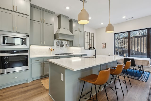 kitchen featuring premium range hood, a sink, appliances with stainless steel finishes, decorative backsplash, and light wood finished floors