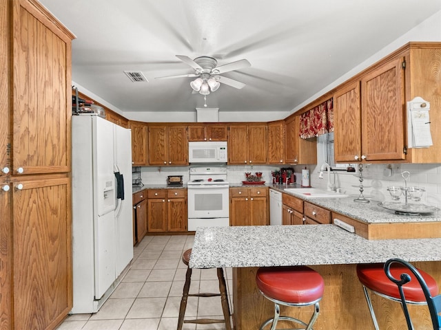 kitchen featuring light tile patterned floors, sink, white appliances, a breakfast bar, and kitchen peninsula