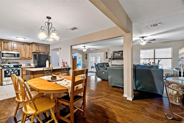 dining area with ceiling fan with notable chandelier, dark wood-type flooring, and a textured ceiling