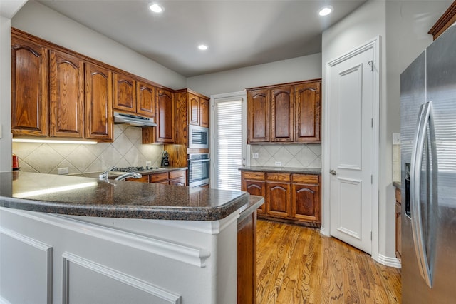 kitchen with decorative backsplash, light hardwood / wood-style flooring, stainless steel appliances, and kitchen peninsula