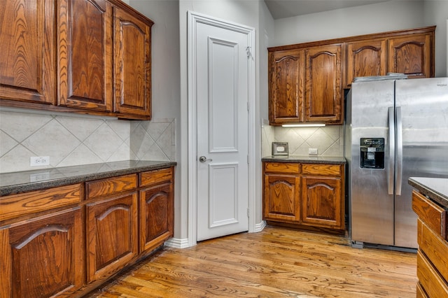 kitchen with backsplash, light hardwood / wood-style flooring, dark stone counters, and stainless steel refrigerator with ice dispenser