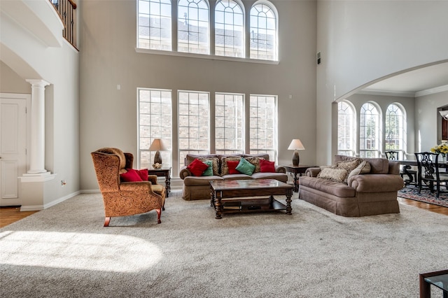 living room with crown molding, decorative columns, light hardwood / wood-style floors, and a towering ceiling