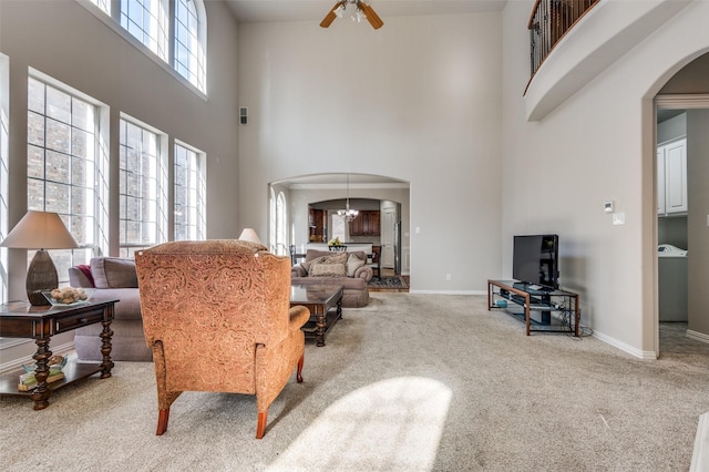 carpeted living room with a high ceiling and ceiling fan with notable chandelier