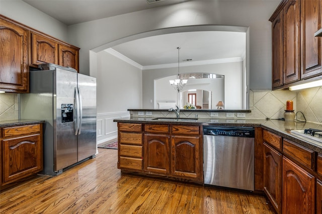 kitchen featuring sink, appliances with stainless steel finishes, hardwood / wood-style floors, ornamental molding, and decorative light fixtures