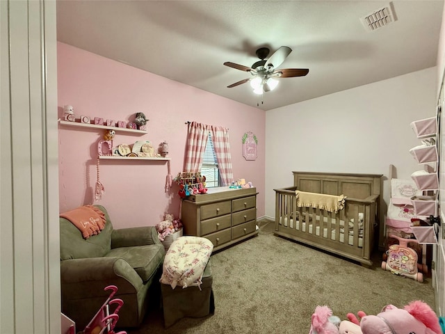 carpeted bedroom with a crib and ceiling fan