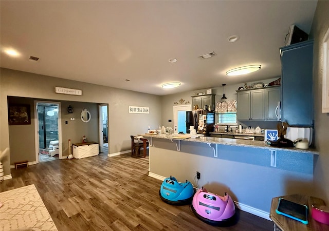 kitchen featuring decorative light fixtures, a kitchen breakfast bar, light stone counters, kitchen peninsula, and dark wood-type flooring