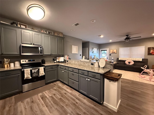 kitchen with gray cabinets, appliances with stainless steel finishes, dark hardwood / wood-style floors, light stone countertops, and kitchen peninsula