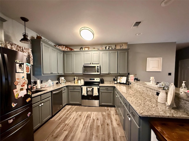 kitchen with light stone counters, decorative light fixtures, gray cabinets, stainless steel appliances, and light hardwood / wood-style floors