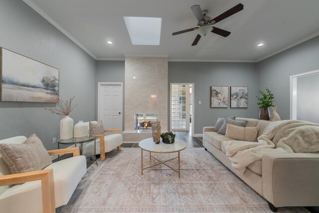 living room with a fireplace, a skylight, hardwood / wood-style flooring, ornamental molding, and ceiling fan