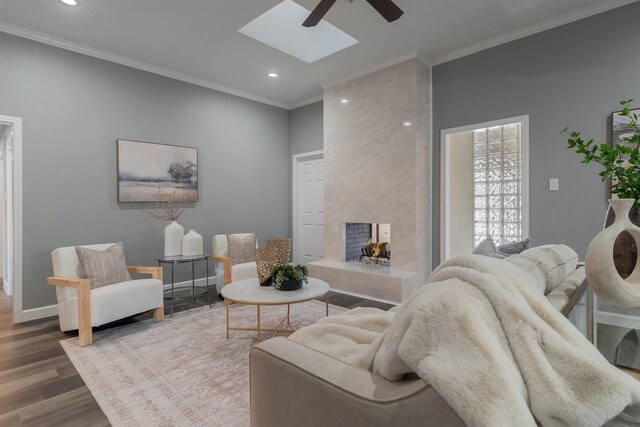 living room featuring wood finished floors, a skylight, crown molding, baseboards, and a tile fireplace