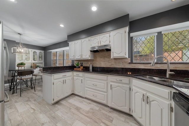 kitchen with under cabinet range hood, a sink, stainless steel dishwasher, a peninsula, and white cabinets