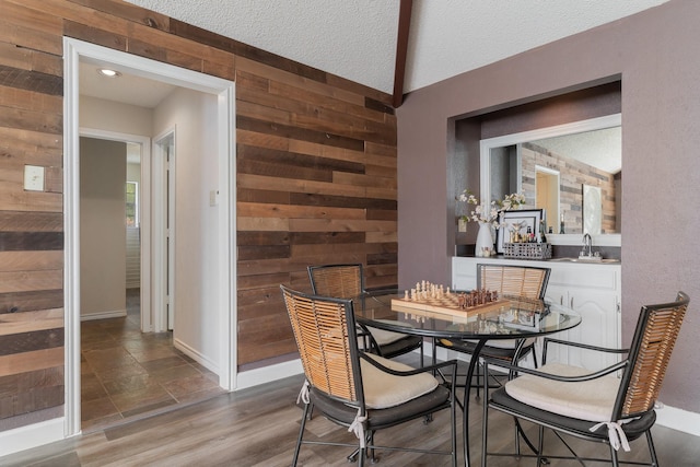 dining space with wooden walls, wood finished floors, baseboards, and a textured ceiling