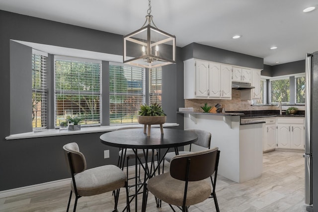 kitchen with freestanding refrigerator, under cabinet range hood, white cabinetry, dark countertops, and backsplash