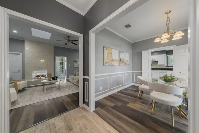 interior space with ceiling fan with notable chandelier, a wainscoted wall, wood finished floors, ornamental molding, and visible vents