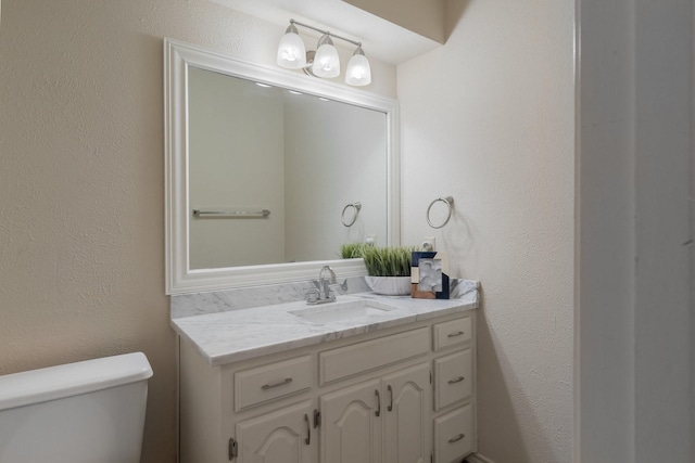 half bath with toilet, vanity, and a textured wall