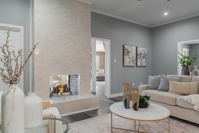 living room with a tile fireplace, crown molding, wood finished floors, and baseboards