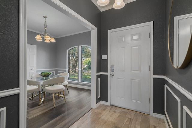 entryway with crown molding, light wood-style floors, a textured wall, and an inviting chandelier
