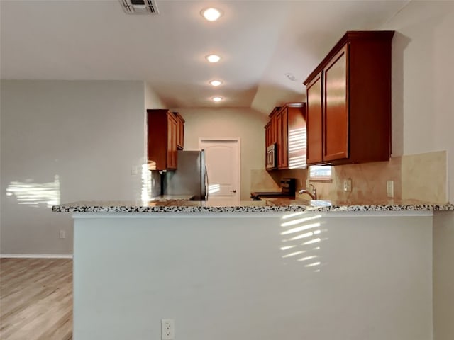 kitchen featuring appliances with stainless steel finishes, backsplash, light stone counters, and kitchen peninsula