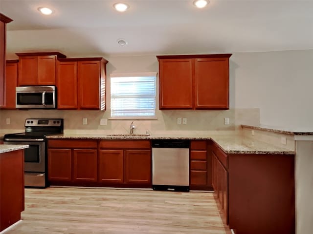 kitchen featuring sink, stainless steel appliances, light hardwood / wood-style floors, light stone countertops, and decorative backsplash