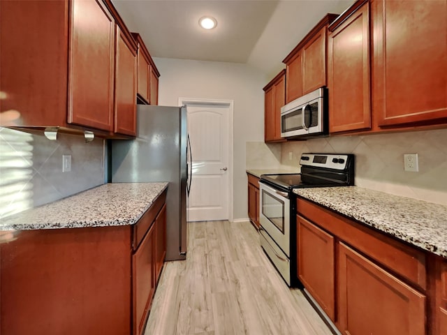 kitchen featuring stainless steel appliances, light stone countertops, backsplash, and light wood-type flooring