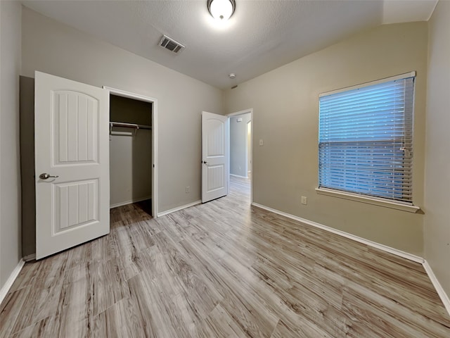 unfurnished bedroom featuring vaulted ceiling, a closet, a textured ceiling, and light wood-type flooring