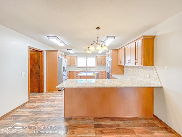 kitchen featuring light wood-type flooring, kitchen peninsula, a chandelier, and decorative backsplash