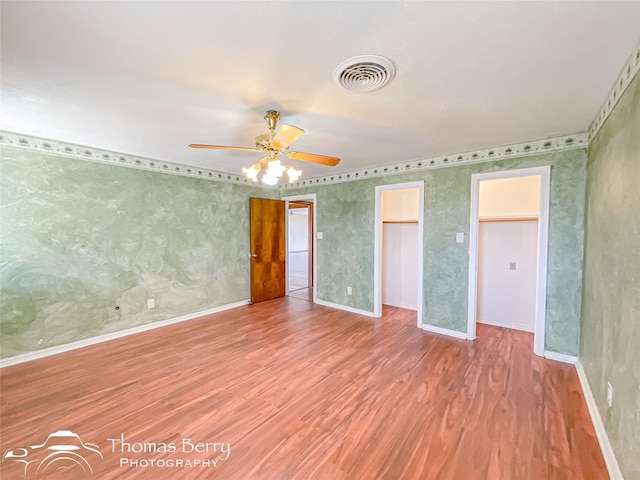 unfurnished bedroom with a walk in closet, ceiling fan, and wood-type flooring