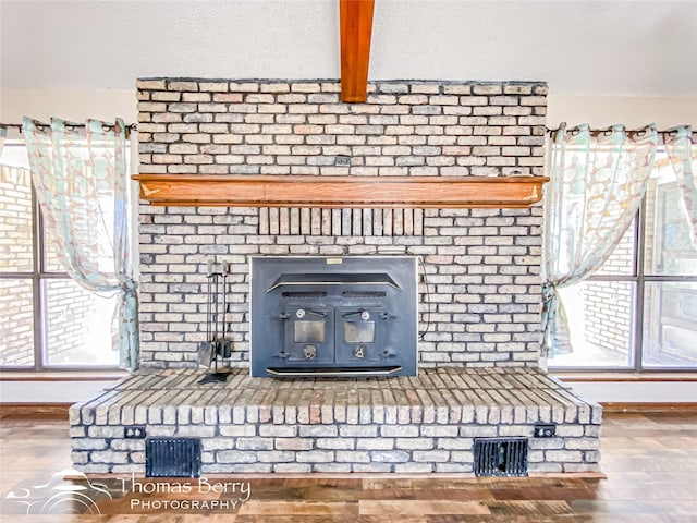 room details featuring a wood stove, wood-type flooring, beamed ceiling, and a textured ceiling