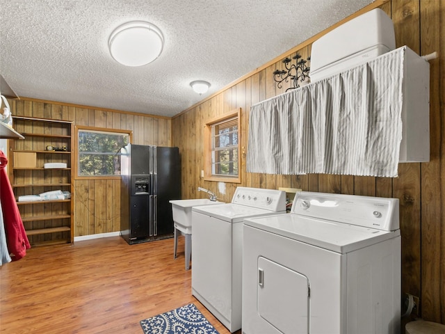 clothes washing area featuring separate washer and dryer, a textured ceiling, wooden walls, and light hardwood / wood-style floors