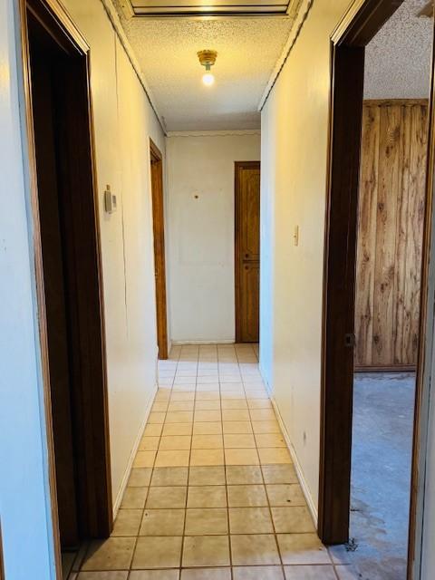 hall featuring wood walls, a textured ceiling, and light tile patterned flooring