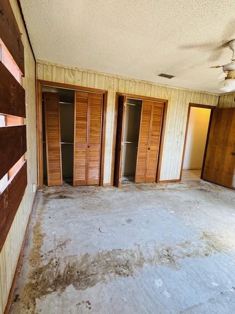 unfurnished bedroom featuring multiple closets, ceiling fan, a textured ceiling, and wood walls