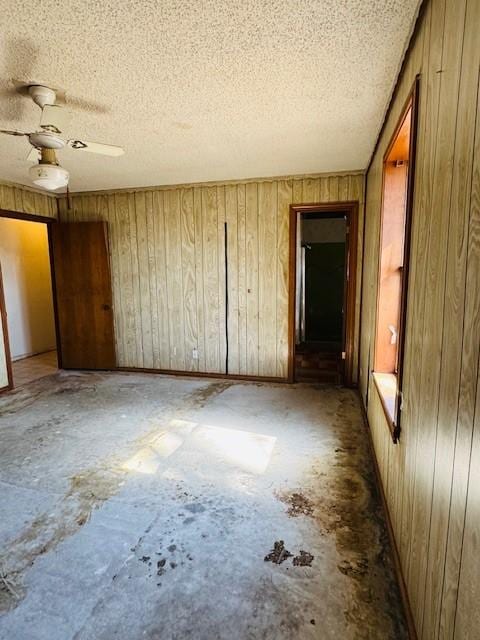 unfurnished bedroom featuring ceiling fan, a textured ceiling, and wood walls