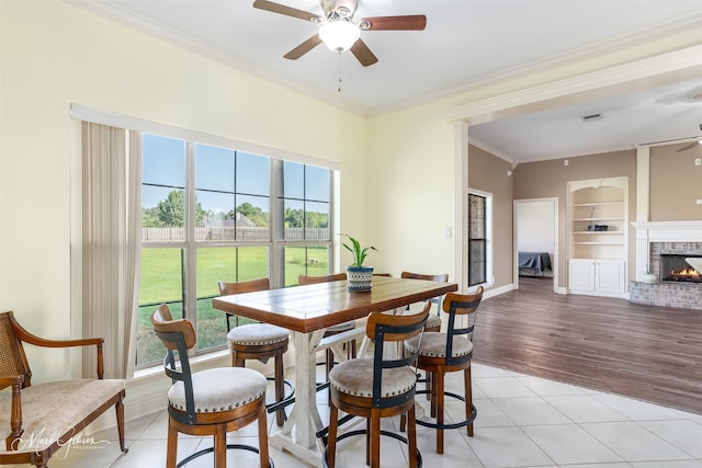 tiled dining space featuring crown molding, ceiling fan, a fireplace, and built in shelves