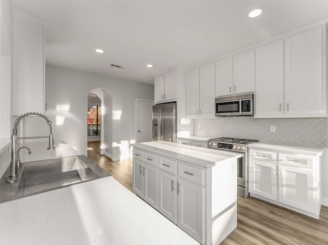 kitchen featuring sink, light hardwood / wood-style flooring, appliances with stainless steel finishes, white cabinets, and backsplash